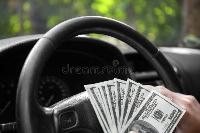 Close-up of american dollars on a wheel. A man driving with money on a car background. Investment and savings concept.