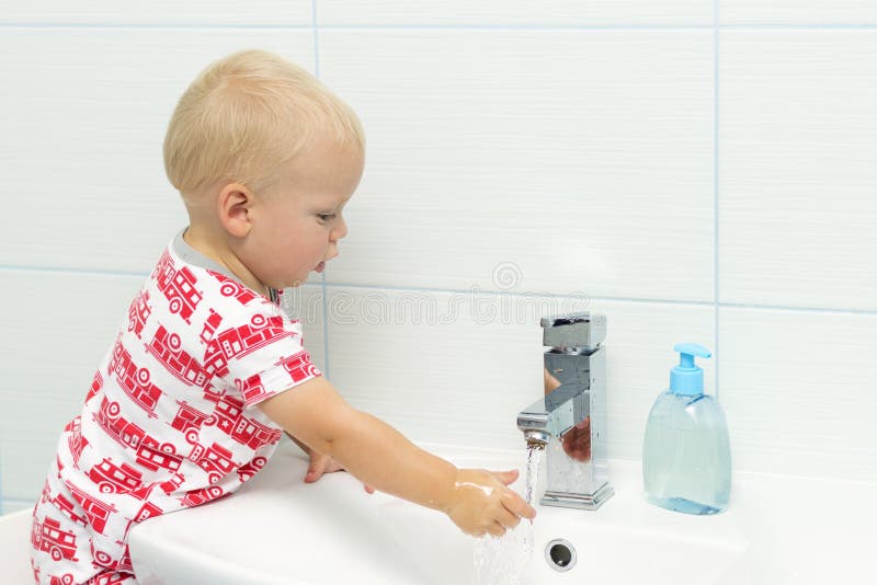 Close-up portrait of adorable white Caucasian boy toddler one year old washing hands in bathroom and looking surprised excited, pl