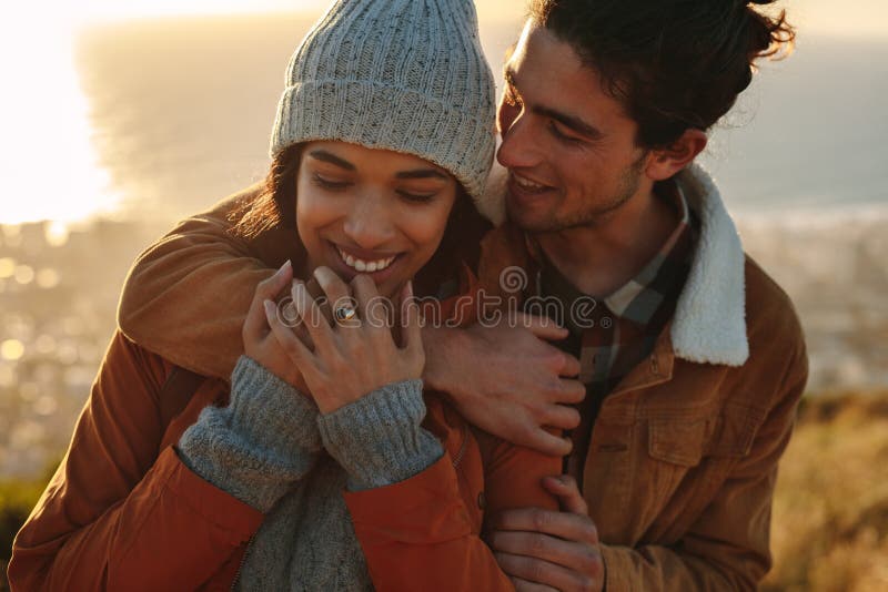 Close up portrait of affectionate young couple on winter holiday. Handsome young men embracing his girlfriend from behind in a winter day. Close up portrait of affectionate young couple on winter holiday. Handsome young men embracing his girlfriend from behind in a winter day.