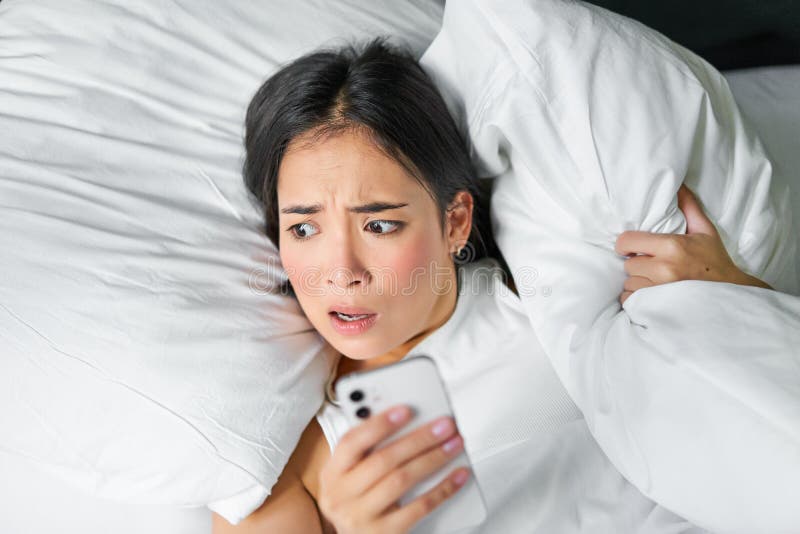 Close Up Portrait Of Asian Girl Lying In Bed Looking At Smartphone