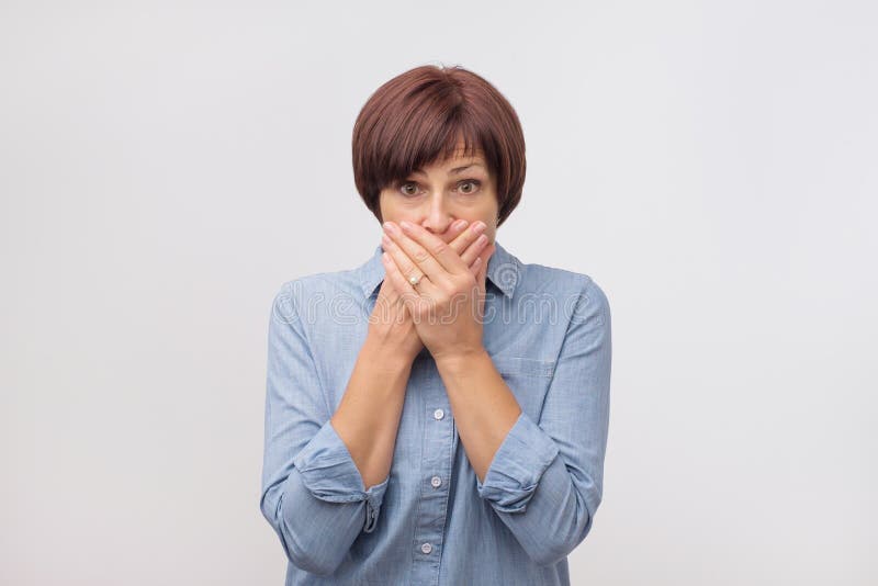 Close up portrait of attractive, mature woman in blue shirt closing her mouth with fingers. She is worried. royalty free stock photo Close up portrait of attractive, mature woman in blue shirt closing her mouth with fingers. She is worried. royalty free stock photo