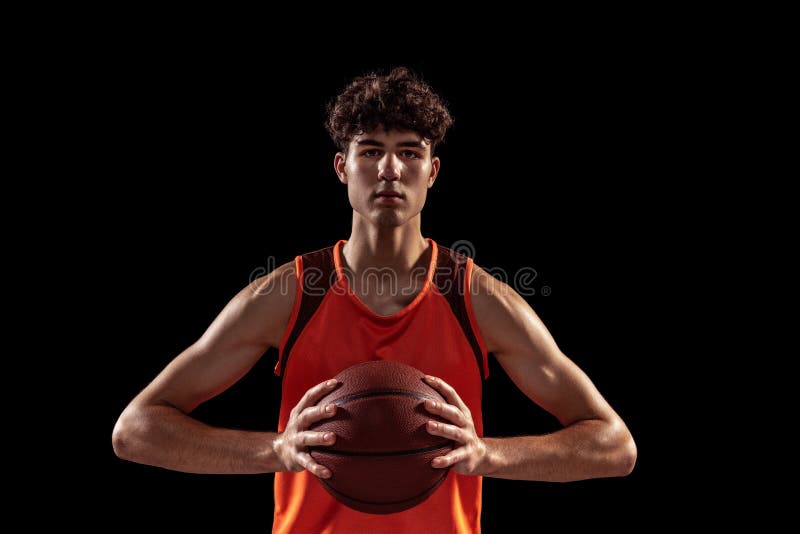 Close-up portrait of basketball player posing with ball isolated on dark studio background. Sport, energy, power