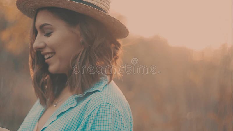 Close-up portrait of a beautiful young girl with long dark hair wearing straw hat. She plays with her hair in the warm