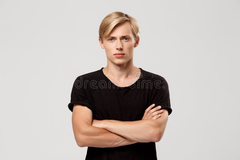 Close up portrait of confident blond handsome young man wearing black t-shirt with hands crossed on chest looking in