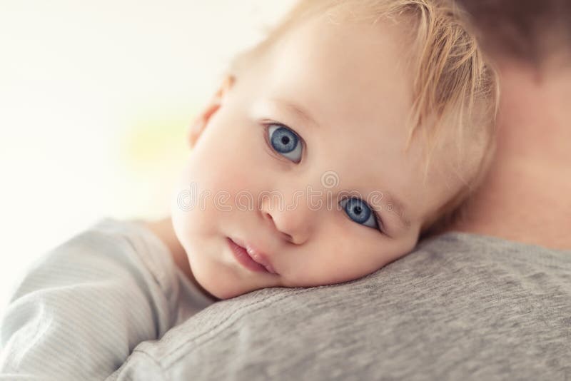 Close-up portrait of cute adorable blond caucasian toddler boy on fathers shoulder indoors. Sweet little child feeling