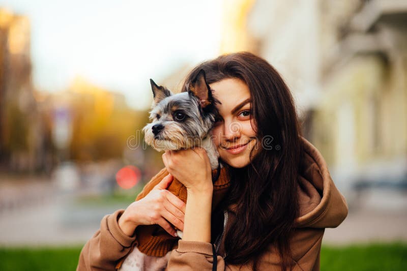 A close-up portrait of a cute lady in casual clothes hugging a small dog on a walk and looking at the camera with a smile on her. Face. Woman hugging a biewer royalty free stock photography