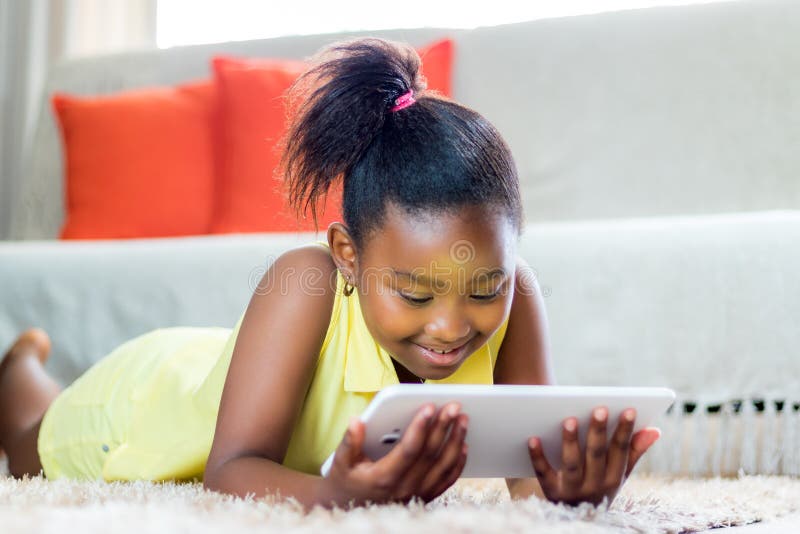 Little african girl playing on tablet in living room.