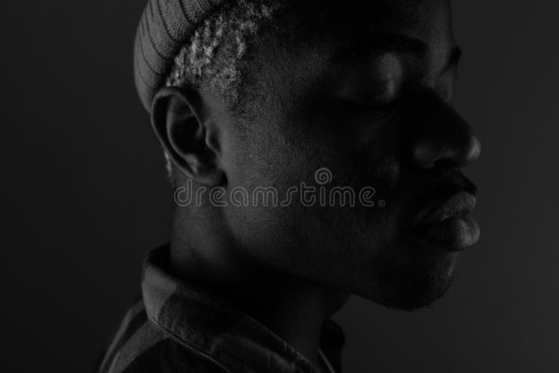 Close-up portrait of a dark-skinned guy with big lips looking sideways in black and white light.