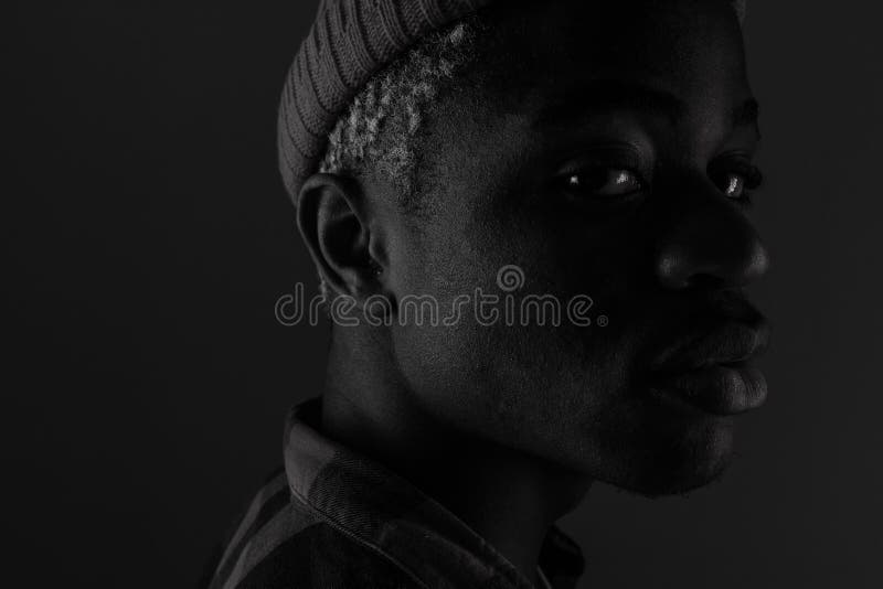 Close-up portrait of a dark-skinned guy with big lips looking sideways in black and white light.