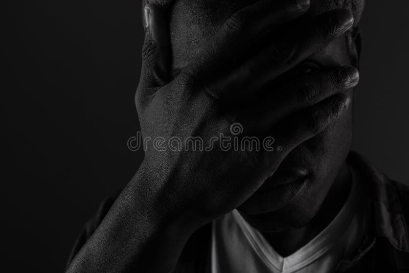 Close-up portrait of a dark-skinned guy with eyes closed by hand in black and white light.