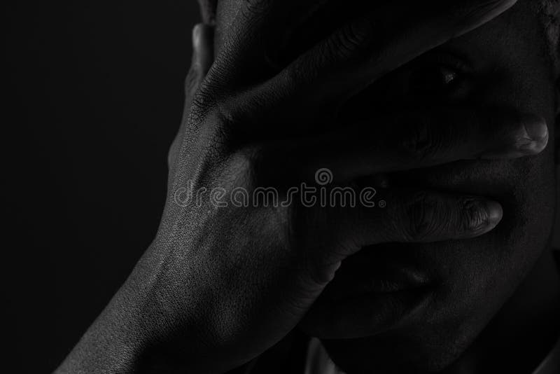 Close-up portrait of a dark-skinned guy with eyes closed by hand in black and white light.