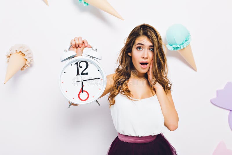 Close-up portrait elegant young woman in stylish dress, posing with white clock on decorated background. Long-haired stock image Close-up portrait elegant young woman in stylish dress, posing with white clock on decorated background. Long-haired stock image