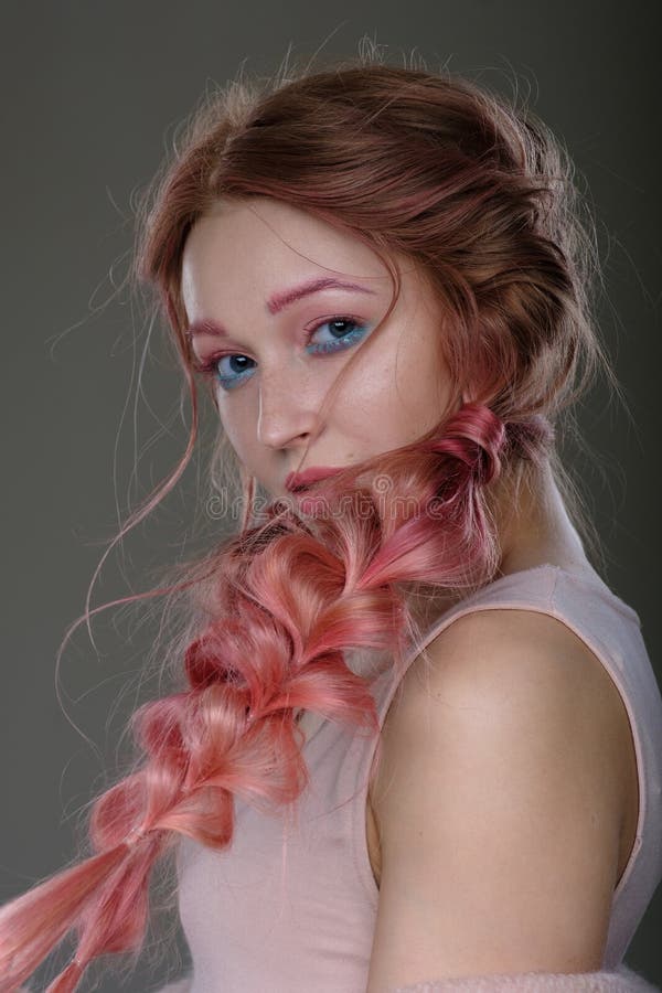 Close-up portrait of girl with pink hair in braids, pink and blue makeup. Girl standing on a dark background, covered his face wit