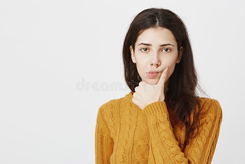 Close-up portrait of gloomy attractive female expressing dislike or boredom, holding hand on ching while thinking about