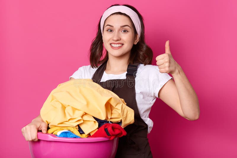 Close up portrait of good looking slender housewife holding pink basin with clean clothes, having positive facial expression, royalty free stock photography Close up portrait of good looking slender housewife holding pink basin with clean clothes, having positive facial expression, royalty free stock photography