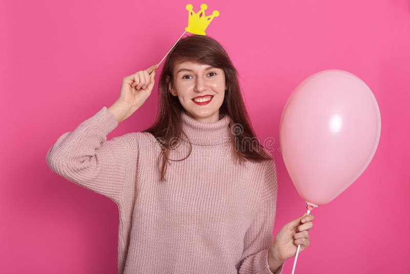 Close up portrait of gorgeous trendy young woman in party outfit and birthday crown, holding rose balloon, posing isolated over stock image Close up portrait of gorgeous trendy young woman in party outfit and birthday crown, holding rose balloon, posing isolated over stock image