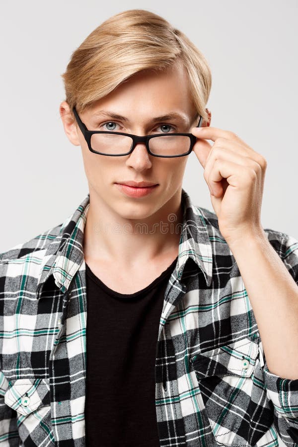 Close up portrait of handsome blond young man wearing casual plaid shirt looking in camera over glasses isolated on grey