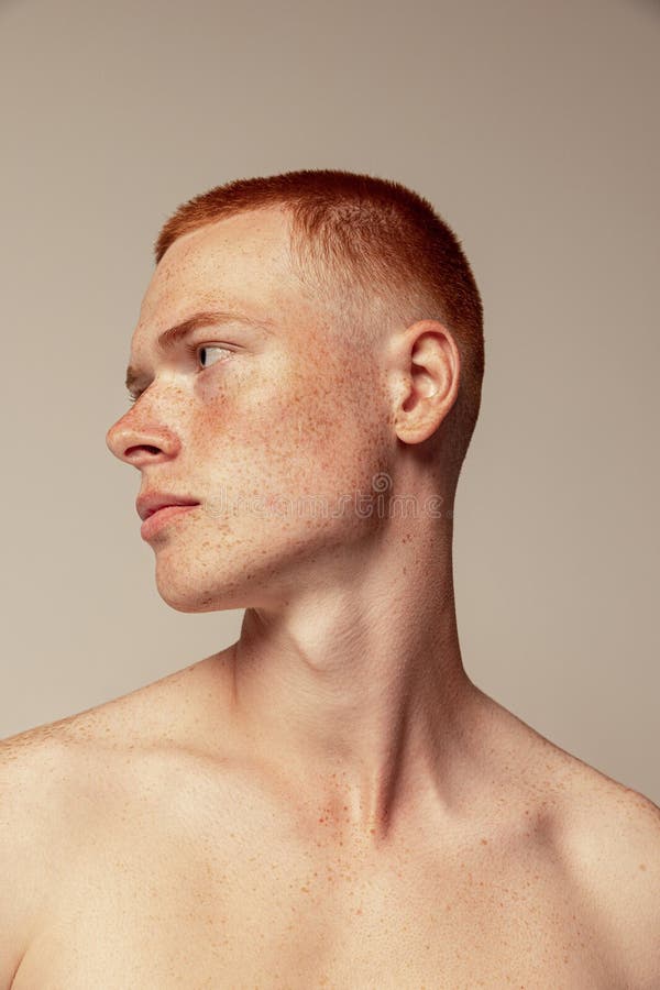 Close-up portrait of handsome young red-haired man posing  over grey studio background