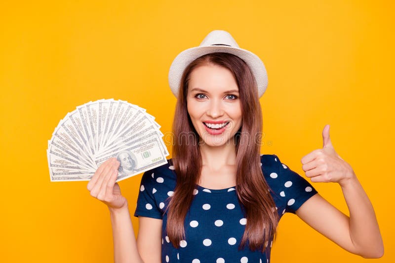 Close up portrait of happy cheerful attractive lucky girl holding money fan in hands near face, having white hat on head, gesture