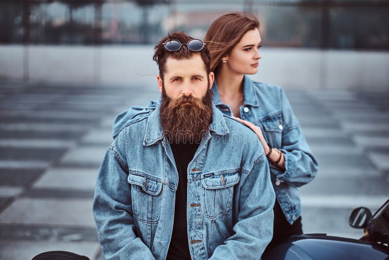 Close-up portrait of a hipster couple of a brutal bearded male and his girlfriend dressed in jeans jackets against stock photo Close-up portrait of a hipster couple of a brutal bearded male and his girlfriend dressed in jeans jackets against stock photo