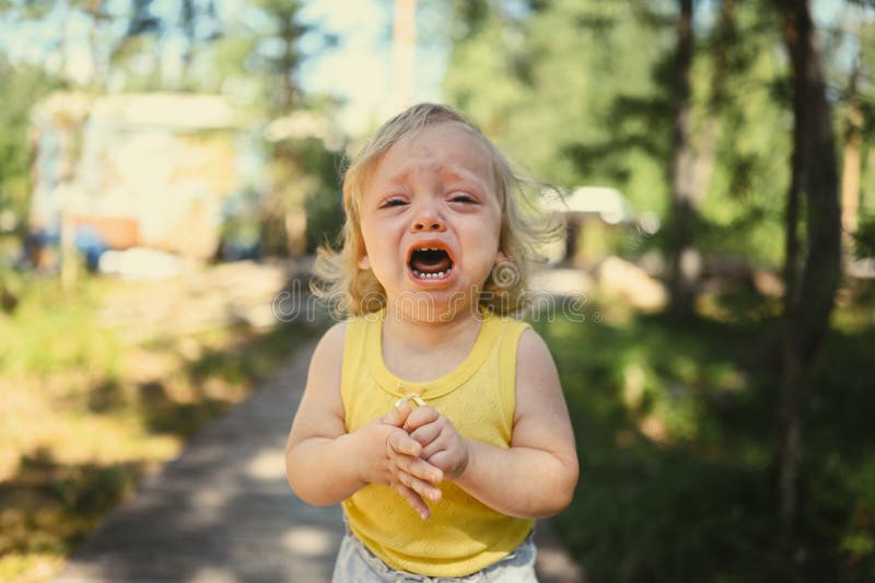 Close up portrait of little funny cute blonde girl child toddler in yellow bodysuit crying outside at summer. Childish