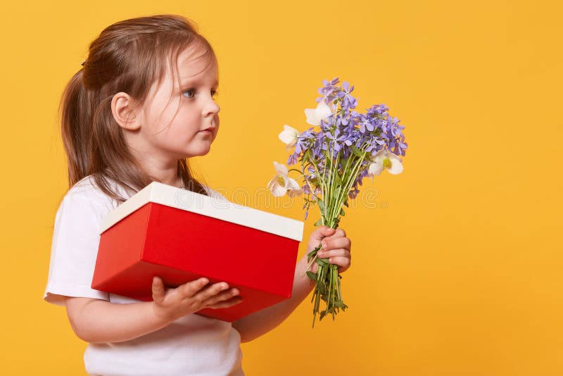 Close up portrait of little girl with red gift box and bouquet of blue florets, preparing to congratulate her mommy with Mother`s