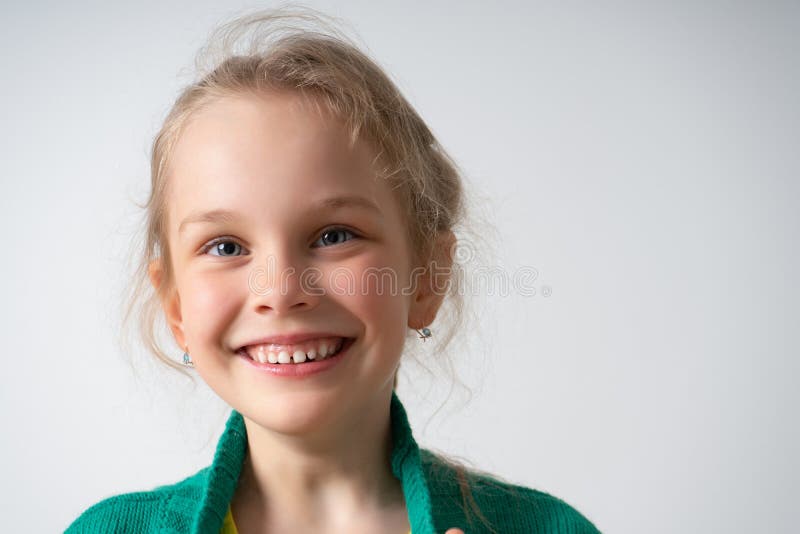 Close up portrait of lovely little girl toughing collar of her sweater with both hands showing happy smile. Studio shot