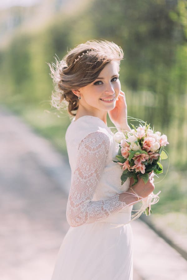 Close up portrait of magical beautiful young bride wearing elegant white dress with bouquet in the park.