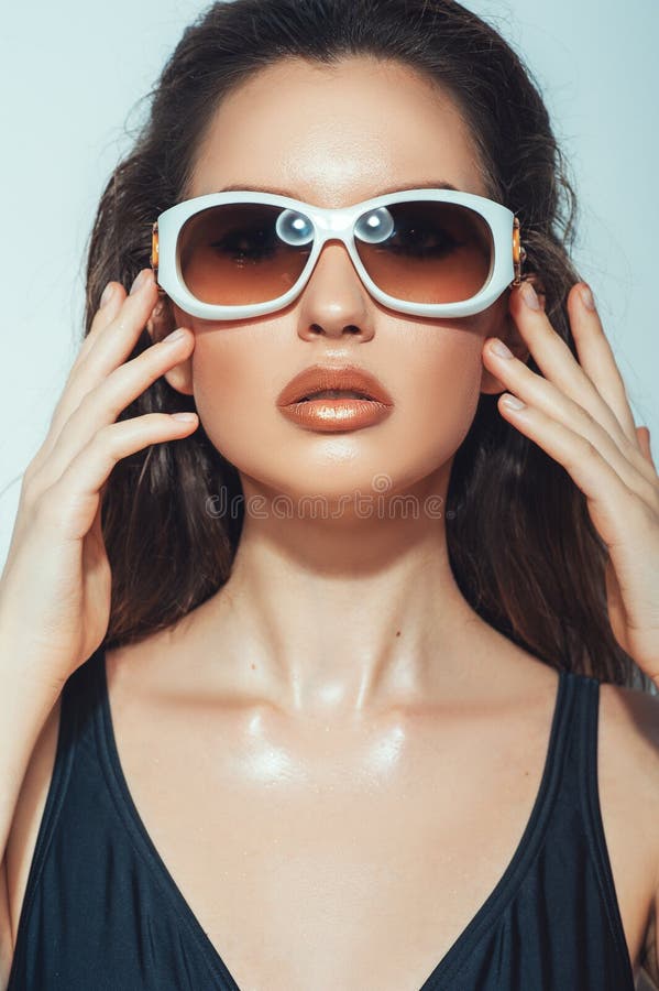 Close up portrait of pretty young woman with white glasses in luxury black bikini. Female fashion model posing with sunglasses.