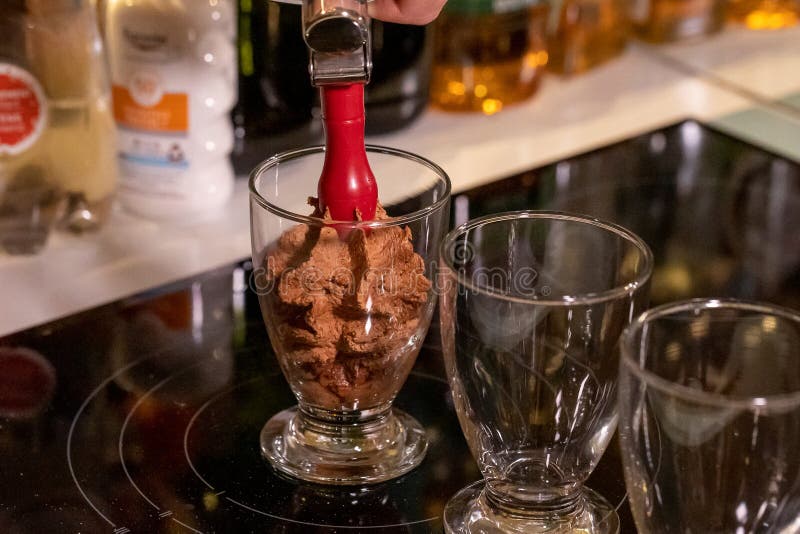 A close up portrait of someone spraying chocolate mousse into glass cups using an espuma device to make it more airy. The dessert