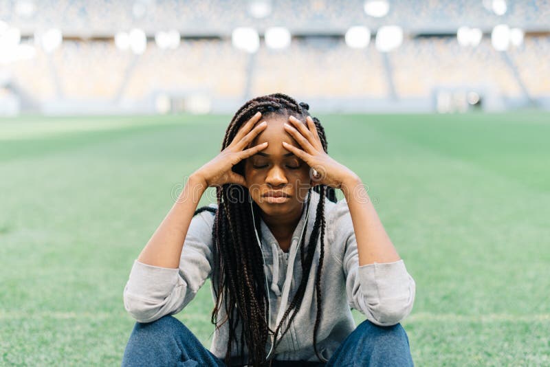 Close-up portrait of the thoughtful afro-american sportgirl sitting on the grass and leaning on the knees. stock image Close-up portrait of the thoughtful afro-american sportgirl sitting on the grass and leaning on the knees. stock image
