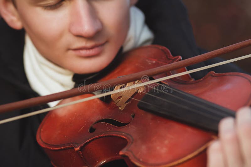 Close-up portrait of a young elegant man playing the violin on autumn nature backgroung, boy`s face with musical instrument under his chin, concept of hobby, art and lifestyle