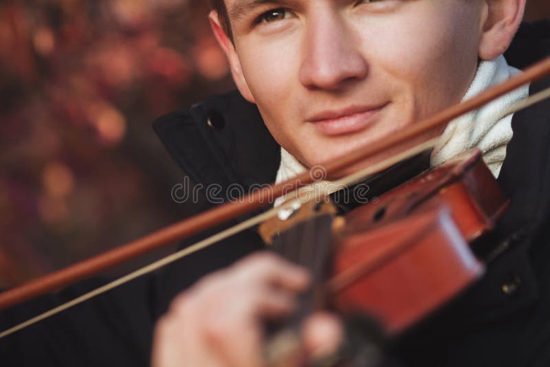 Close-up portrait of a young elegant man playing the violin on autumn nature backgroung, boy`s face with musical instrument under his chin, concept of hobby, art and lifestyle