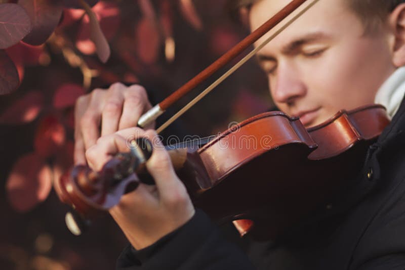 Close-up portrait of a young elegant man playing the violin on autumn nature backgroung, boy`s face with musical instrument under his chin, concept of hobby, art and lifestyle