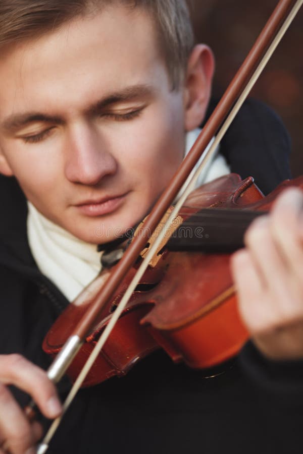 Close-up portrait of a young elegant man playing the violin on autumn nature backgroung, boy`s face with musical instrument under his chin, concept of hobby, art and lifestyle