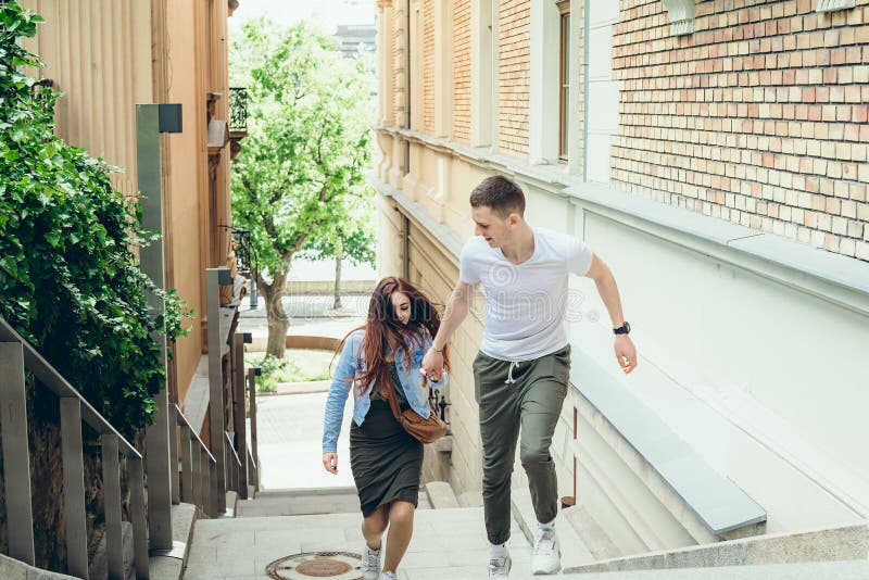 Close-up portrait of the young pretty loving couple holding hands while going up the stairs in the narrow Budapest stock photo Close-up portrait of the young pretty loving couple holding hands while going up the stairs in the narrow Budapest stock photo