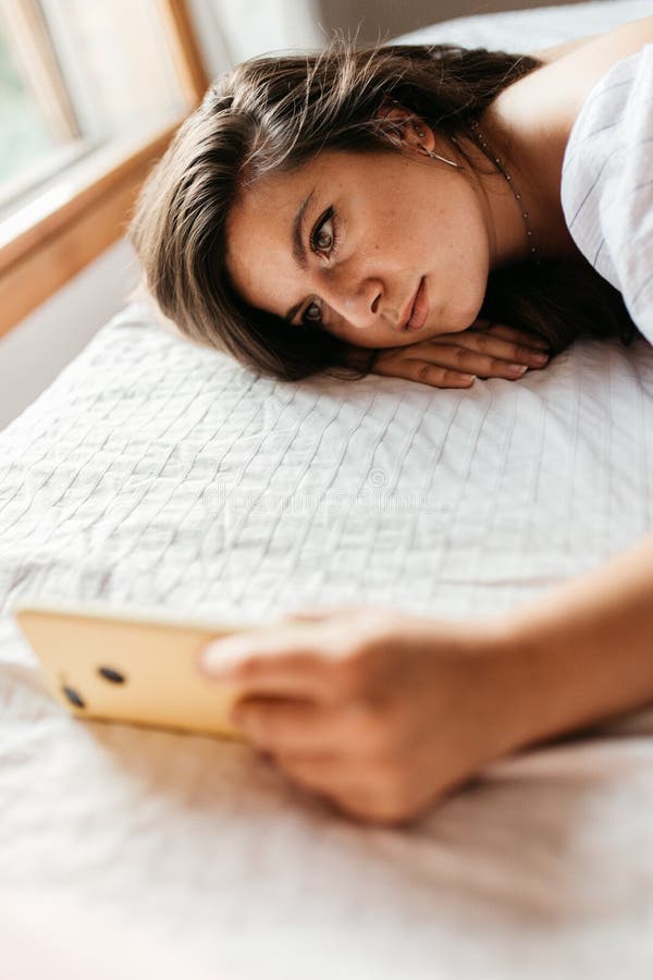 Close up portrait of young sad woman lying on the bed looking at her smartphone feels unhappy. Waiting for mobile message. Feeling