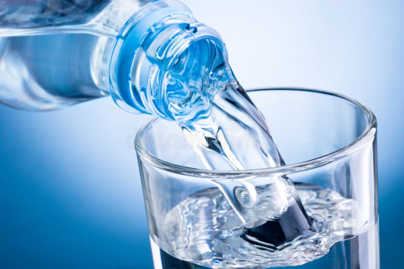 Close-up pouring water from bottle into glass on blue background stock image Close-up pouring water from bottle into glass on blue background stock image