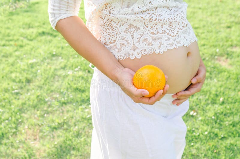 Close up pregnant belly holding oranges in hand. 