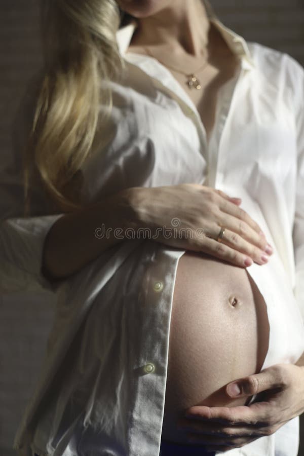 Close-up of a pregnant woman in a white shirt, gently stroking her stomach with her hands in the late stages of pregnancy. Waiting for the baby. High quality photo