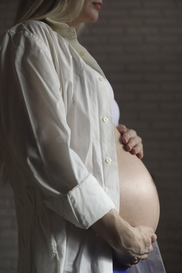 Close-up of a pregnant woman in a white shirt, gently stroking her stomach with her hands in the late stages of pregnancy. Waiting for the baby. side view. High quality photo