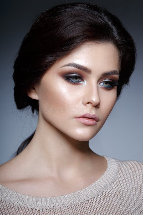 Close up profile portrait of a graceful young woman with perfect makeup and fresh skin,  on a grey background.