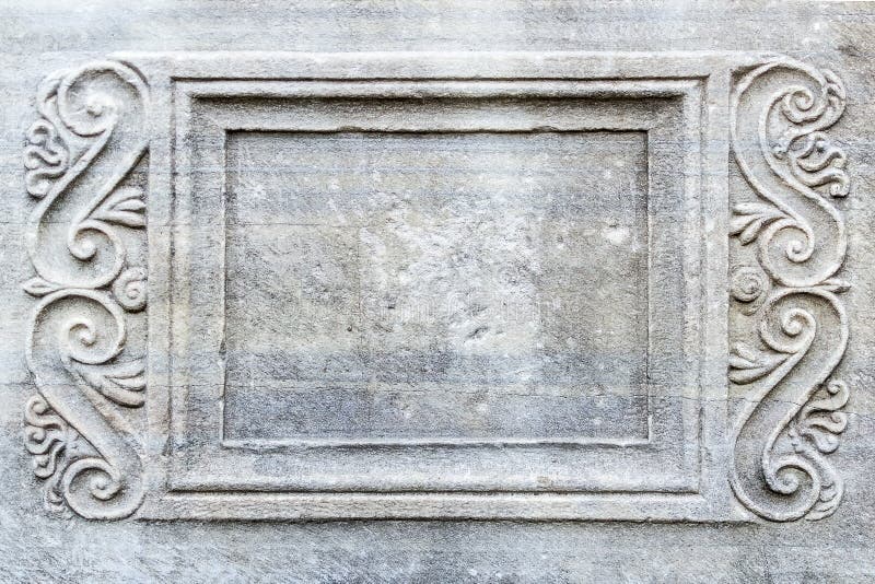 Close-up of rectangular frame with engraved ornament on ancient stone sarcophagus in a public park.