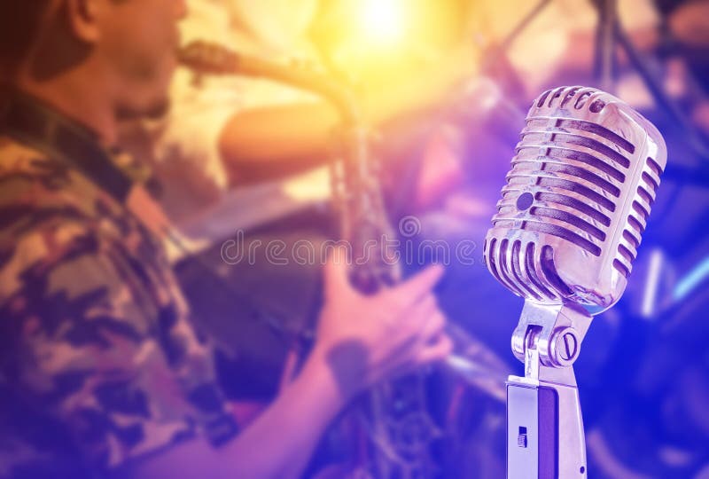Close up retro microphone with musician playing saxophone on band in nigh concert background stock image