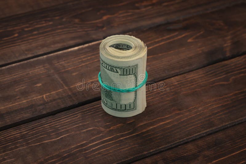 Close-up roll of one hundred dollar bills tied with a green elastic band on brown wooden background, bundle of money is a business stock images Close-up roll of one hundred dollar bills tied with a green elastic band on brown wooden background, bundle of money is a business stock images