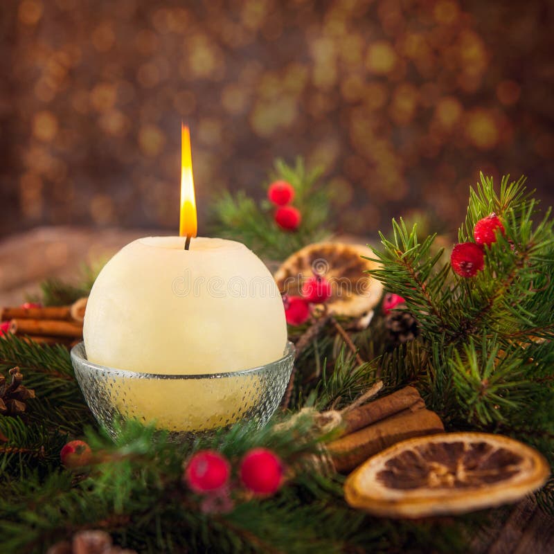 Close up round ivory burning Christmas candle on advent wreath with natural decor on the old rustic table with blurred luminous ba