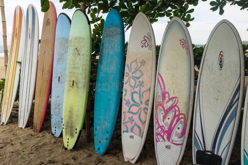 A close up of a row of multi-coloured surf long boards lined up for hire on a beach at Puerto Viejo de Talamanca in