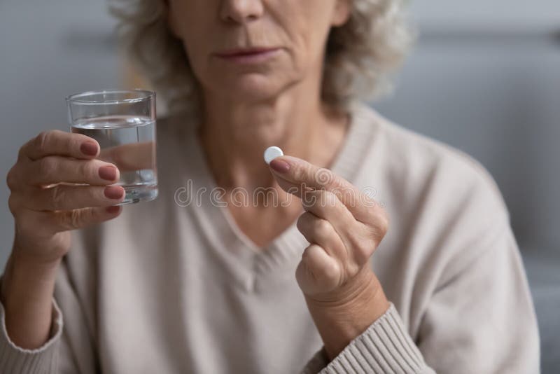 Closeup view senior woman holding glass of water and pill