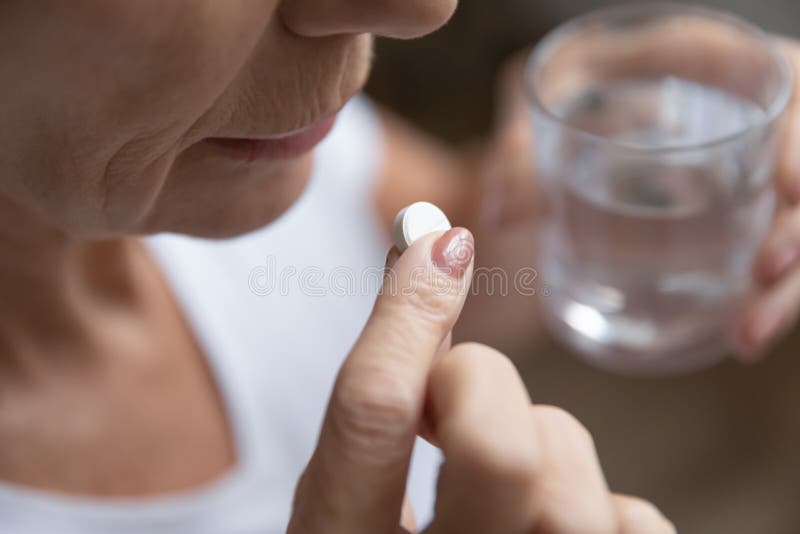 Close up senior woman taking pill, holding glass of water