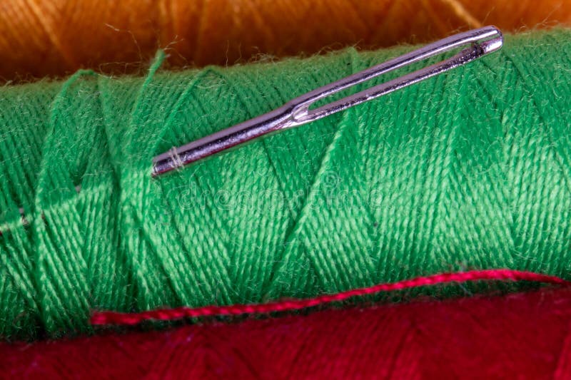 Close-up of sewing needle on green thread spool with red background. royalty free stock images